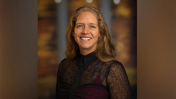 Phoebe Elefante, a woman with shoulder-length light brown hair and a black blouse smiling in front of an out-of-focus brown backdrop.