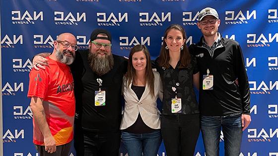 Armada graduates Nathan Duke and Megan Danaher and Full Sail esports staffers Sari Kitelyn, Bennett Newsome, and Jacob Kaplan stand in front of a NACE backdrop.