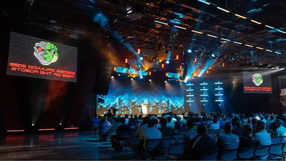 Attendees sit in the 满帆 Live venue. Screens with a lizard robot logo and the words BSides Orlando 2023: Rise of the Robots are on either side of the stage.