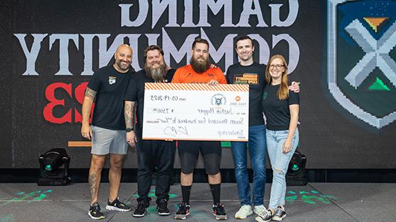 山姆·卢波, DrLupo, 班尼特新闻ome, and Kevin Murray on stage in the Fortress with a student in an orange Armada jersey receiving an oversized scholarship check.