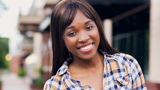 Brandie Green smiles at the camera. She is standing outdoors and wearing a flannel button-down shirt.