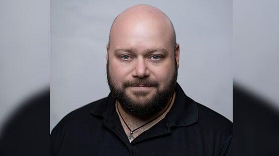 Grad Corey Guerra is wearing a black polo shirt and posing for a headshot against a light grey backdrop.