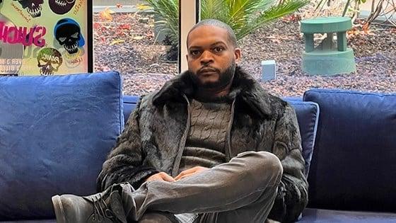 Terique Walker sits on a blue sofa wearing a black fur coat and turtleneck.