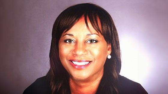 Lorraine smiles at the camera. She has dark brown hair and hazel eyes and is wearing a blue blazer and silver earrings.