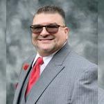 Will Torres wears a gray pinstriped suit with a red tie, a red carnation on the lapel, and sunglasses.