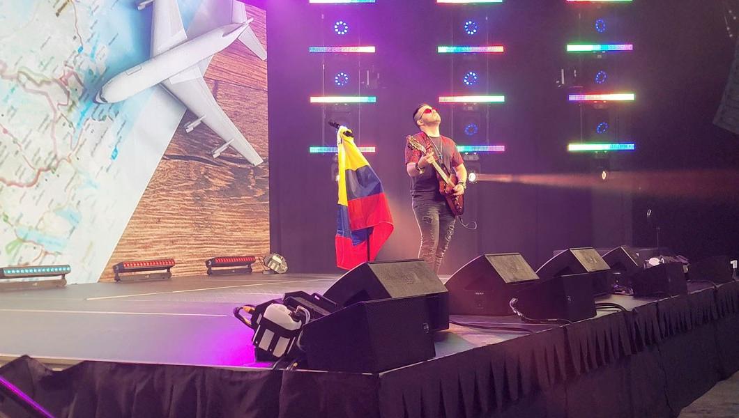 A person is on stage and playing the guitar with the Colombian flag on a flag pole beside them.