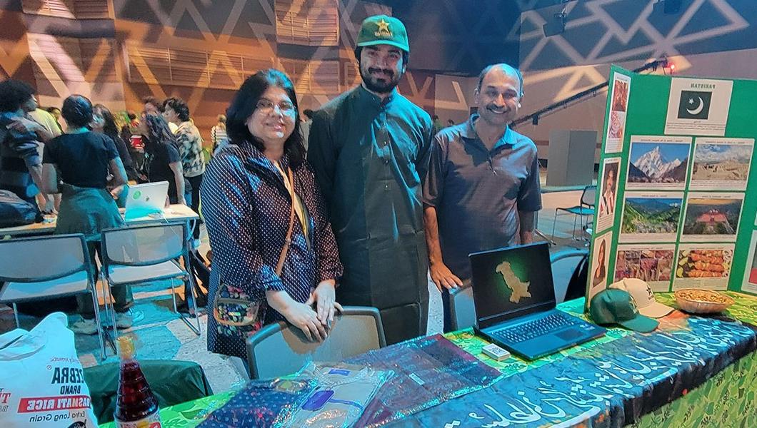 A group of three people standing behind a table representing Pakistan at a cultural festival.