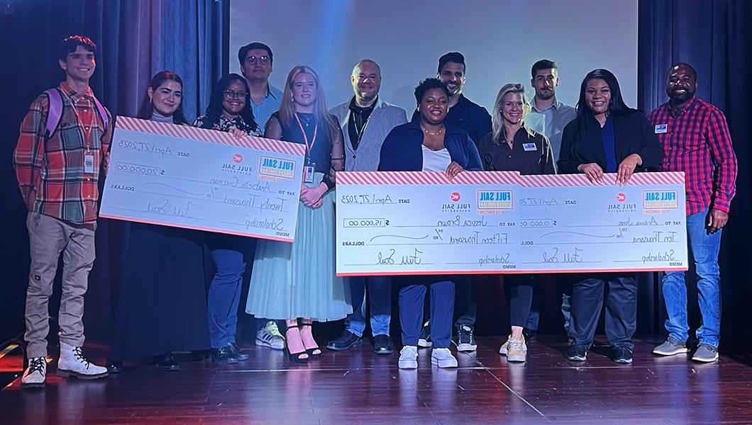 The finalists, participating faculty, and judges stand together. The three winners are holding over-sized checks. Everyone is smiling.